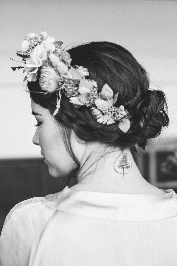 Braut von hinten beim Getting Ready mit lockerer Hochsteckfrisur und Blumenkranz
