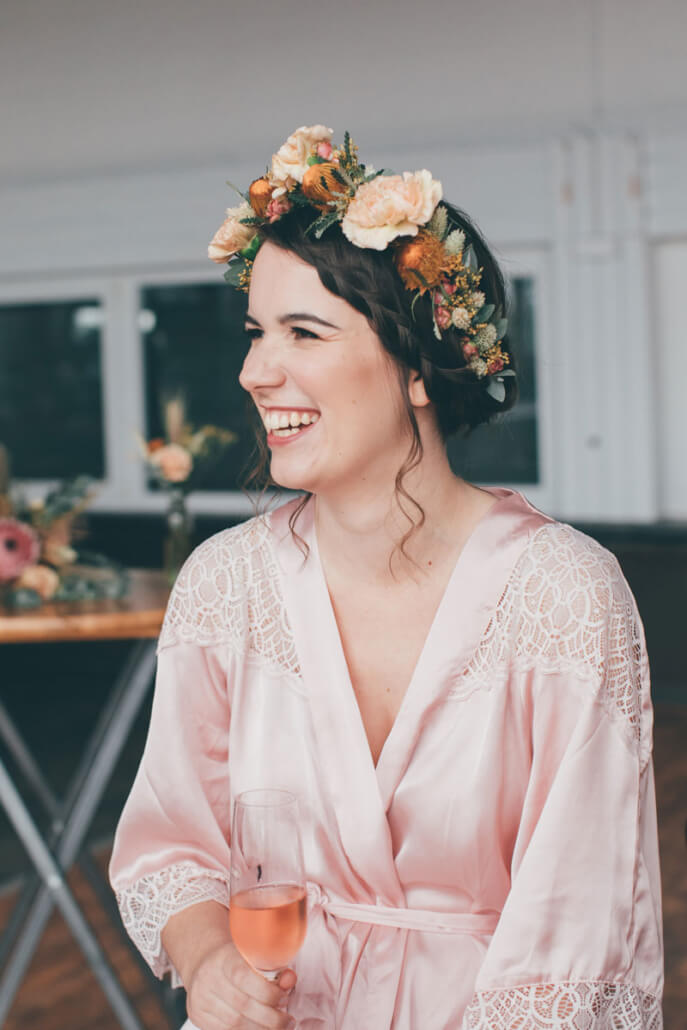 lachende Braut beim Getting Ready mit Blumenkranz und Morgenmantel